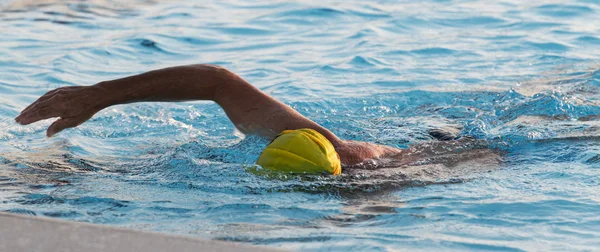 Man swimming in outdoor pool with yellow bathing cap