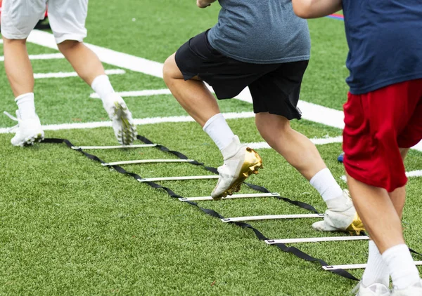 Three athletes in cleats doing ladder foot drills on turf field — Stock Photo, Image