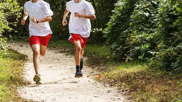 Dois corredores em camisas brancas e shorts vermelhos na floresta — Fotografia de Stock