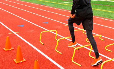 Bir lise atletizm takımının arka görüntüsü kırmızı bir pistte sarı engelli koşuyor..