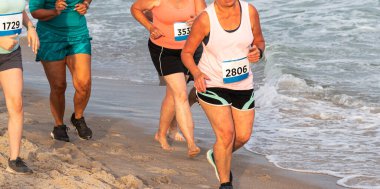A group of women running a one mile race on the sand at the edge of the water at Rober Moses State Parks beach. clipart