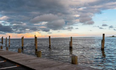 Büyük Güney Körfezi 'ndeki bir rıhtımda güneşin turuncu bulutlarıyla birlikte kara bulutlar süzülüyor..