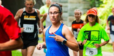 Babil, New York, ABD - 12 Ağustos 2018: Bir grup insanın içinde bir tünelde koştuktan sonra ormanda 10K koşan bir kadın koşucu barış işareti veriyor.