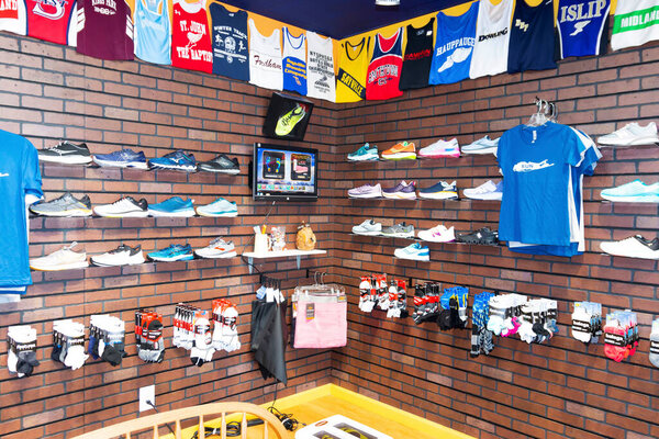 Smithtown, New York, USA - 28 August 2020: Running shoes are on display with clothing and uniform tops hanging on the wall at a local running shoe store.