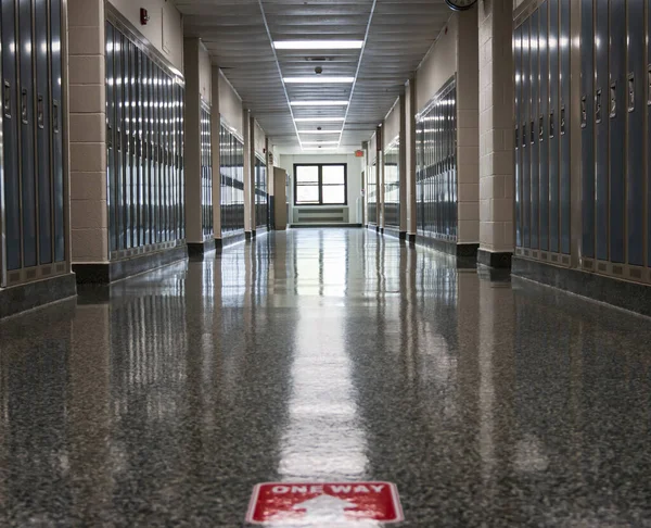 An empty high school hallway with one way sign taped on the floor as part of the neew normal for opening up schools in a pandemic.
