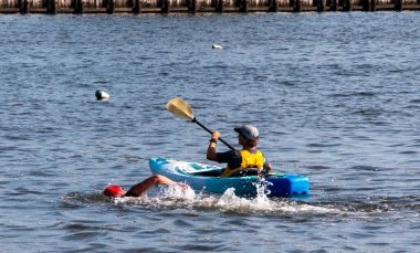Parlak twaters, New York, ABD - 14 Temmuz 2022: Bir kanocu antrenman sırasında yakınlardaki bir yüzücüyü gözlemleyerek sakin sularda sorunsuzca süzülüyor.