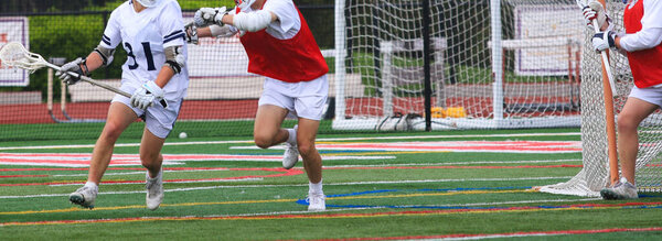 Players in white uniforms competing agians players in Red during a lacrosse Game. 