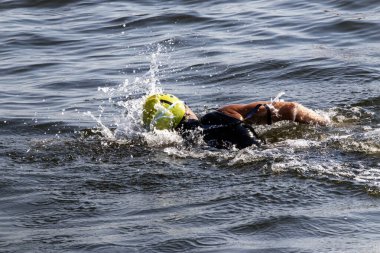 Bir yüzücü açık suda idman yapar, her vuruşta sarı bir yüzme şapkası takar..
