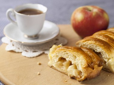 Bir elma ve bir fincan kahve ile dilimlenmiş elmalı turta masada yatıyor