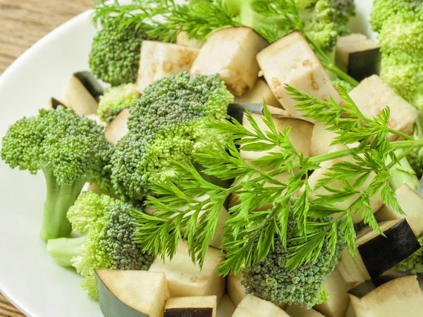 Col de brócoli en rodajas se encuentra en un plato con trozos de berenjena sobre la mesa — Foto de Stock