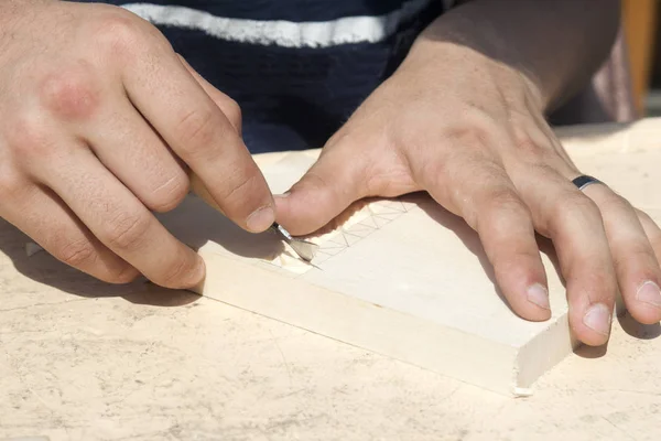 Un hombre corta un patrón con un cuchillo en una superficie de madera — Foto de Stock