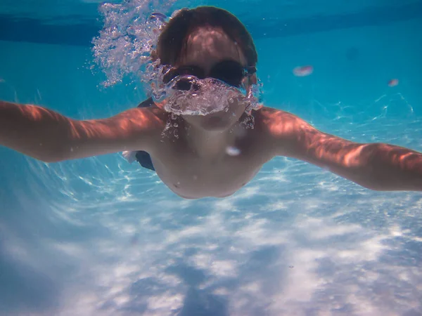 Genç bir çocuk su altında yüzer ve kabarcıklar üfler.