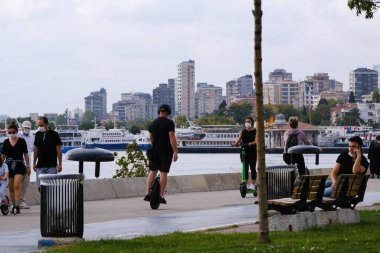 İstanbul, Türkiye - 13 Eylül 2020: İnsanlar İstanbul 'un Bostancı ilinin Kadiköy kıyısında yüz maskeleriyle elektrikli scooter ve bisiklete biniyor. Bir adam elektrikli tek tekerlekli bisiklete biniyor..