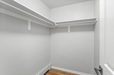 Beyaz duvarları ve rafları olan küçük, boş bir dolap. Mekan dağınık ve temiz, sakinlik ve düzen hissi veriyor.