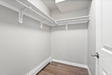 Beyaz rafları olan küçük, boş bir dolap. Kapı açık ve zemin tahtadan yapılmış.