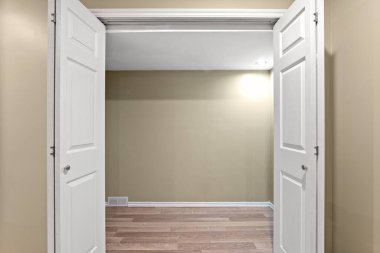 İki kapısı açık, geniş, boş bir oda. Oda çıplak ve dağınık, görünür mobilya ya da dekorasyon yok. Açık kapılar geniş bir izlenim veriyor.