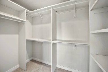 Rafları ve beyaz duvarı olan beyaz bir dolap. Dolap boş ve hiç giysisi yok. Dolap çok temiz ve düzenli.