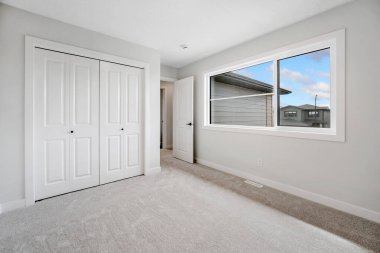 Penceresi ve beyaz kapısı olan yatak odası. Oda boş ve minimalist bir görünüşü var.