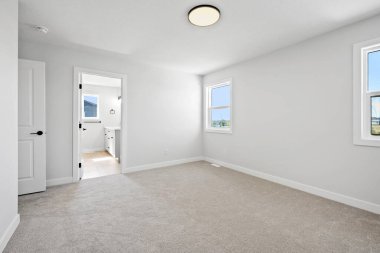 Beyaz kapısı ve beyaz duvarı olan büyük, boş bir oda. Oda çıplak ve dağınık. Mobilya ya da dekorasyon yok. Pencerelerden gelen ışık mekanı aydınlatıyor, aydınlık hissettiriyor.