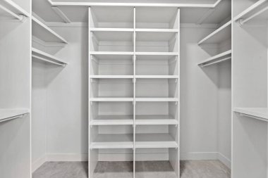 Beyaz rafları olan büyük, boş bir dolap. Boş alan, temiz, düzenli ve geniş bir alan izlenimi veriyor. Dolabın ve rafların beyaz rengi basitlik hissi yaratıyor.