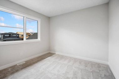 Very clean and empty bedroom with a large window. The room is very bright and airy, with a view of the outside