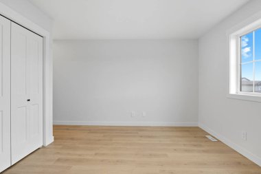 White room with a window and a closet. The walls are white and the floor is wooden