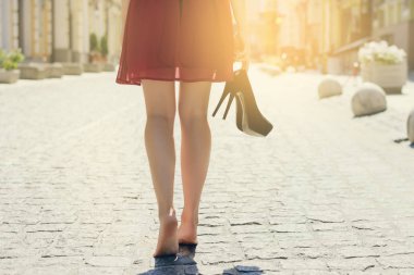 Woman in dress, high heel shoes hand, walking in city barefoot. Close up cropped rear behind back view photo of woman's legs. Sun beam light rays shine sunburst burst  shiny flare effect glare sparkle clipart