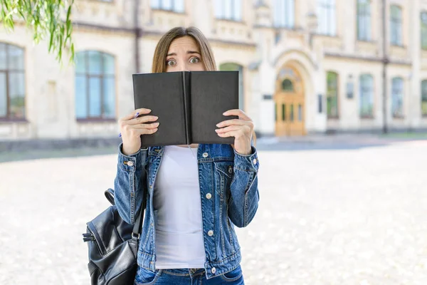 Not ready for exam! Entrance person people insane anxiety emotion facial expression concept. Photo portrait of frightened crying smart clever girl looking at camera hiding behind opened book