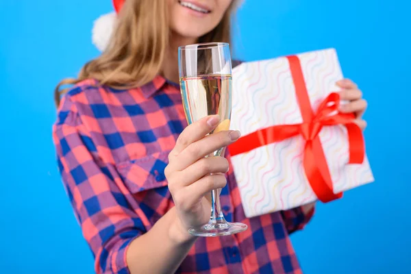 Concept of having an office party before New Year and Christmas. Woman\'s hand holding a glass of champagne, present box is on the vivid blue background