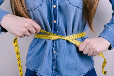 BMI boyutu ölçek açlık açlık kavramı. Kırpılan closeup fotoğraf mutsuz, yorgun yorgun depresif vurguladı o ince sarı Cetvelin santimetre avuç içi izole gri arka planda tutarak onun Bayan