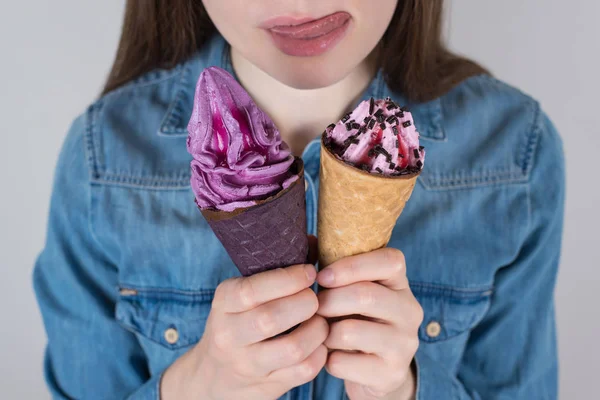 Cropped closeup photo of slimming lady can not stand trying to eat all sweets from fridge holding both delicious pastry with sprinkles in hands isolated grey background