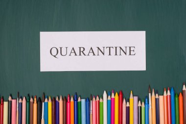 Tecrit konsepti. Ev konseptinde ders çalışmak. Yukarıdaki karantina kağıdının resmi ve yeşil tahta üzerinde izole edilmiş renkli boya kalemleri.