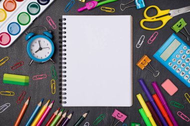 Eğitim konsepti. Yukarıda, tahtada izole edilmiş çok renkli kırtasiye malzemeleriyle çevrili boş defterin yukarıdaki görünüm fotoğrafı
