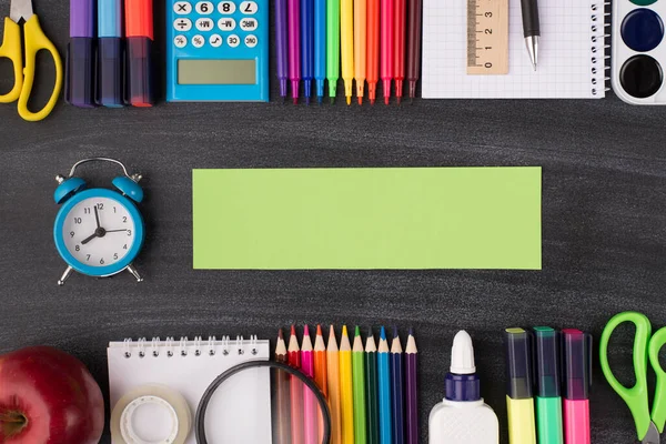 Task deadline concept. School project concept. Top above overhead view photo of clock with green note beside and colorful stationery above and below it isolated on blackboard with copyspace