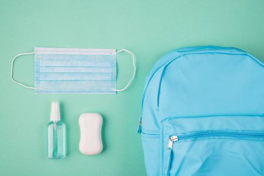 Coronavirus salgını konsepti. Sağlık sigortası konsepti. Yukarıda mavi sırt çantalı sabun ve el dezenfektanının turkuaz arka planda izole edilmiş fotoğrafı var.