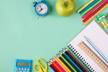 Okul konseptine geri dönelim. Üst tepede renkli okul kırtasiyesinin resmi mavi saat ve elmanın kopyalanmış turkuaz zemin üzerinde izole edilmiş.