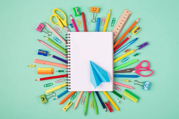 Top above overhead view photo of multicolored stationery and blank notebook with blue paper plane isolated on turquoise background