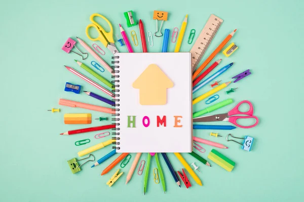 Studying at home concept. Top above overhead view photo of colorful stationery and blank notebook with house shaped paper and home letters on top isolated on turquoise background