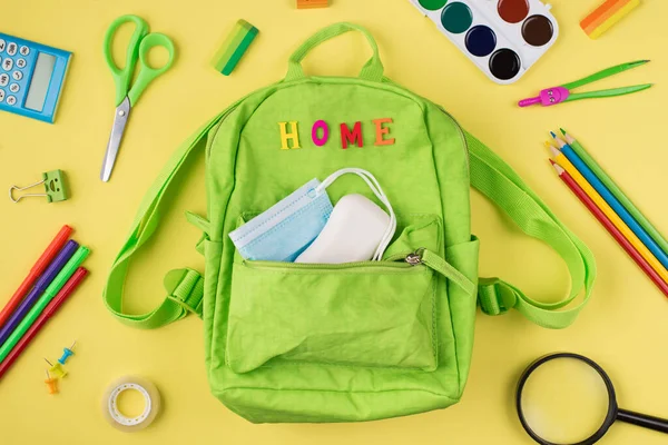 Studying at home concept. Top above overhead view photo of green backpack mask soap and colorful stationery isolated on yellow background