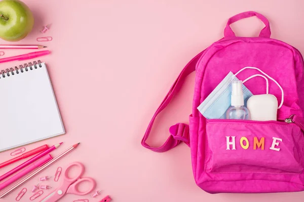 Studying at home concept. Top above overhead flat lay view photo of pink backpack with mask, sanitizer and soap and pink stationery isolated on pastel pink background with copyspace