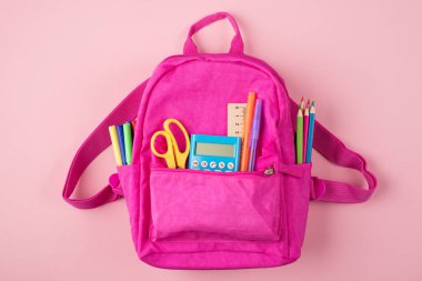 Okul konseptine geri dönelim. Üstünde pembe sırt çantasının resmi ve renkli kırtasiye malzemesi var, pastel pembe arka planda izole edilmiş.