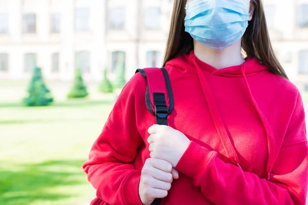Normal life using face mask concept. Cropped close up photo portrait of serious girl in casual red pullover and filter mask standing near school building