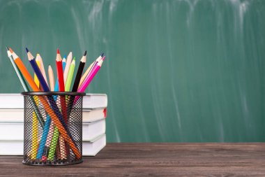 Okul eğitimi konsepti. Renkli boya kalemlerinin yakın plan fotoğrafı ve yeşil karatahta kopyalama alanı üzerinde izole edilmiş ders kitapları yığını