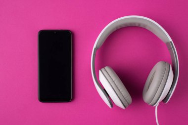 İletişim konsepti. Üstünde pembe arka planda izole edilmiş telefon ve kulaklıkların resmi var.