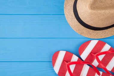 Tatil zamanı konsepti. Üstünde çizgili terliklerin ve şapkanın fotosu var. Mavi ahşap arka planda izole edilmiş ve kopyalanmış.