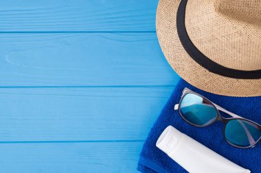 Yaz tatili konsepti. Yukarıda yukarıda havlunun yakın plan fotoğrafı güneş gözlüğü ve güneş kremi mavi ahşap arka planda izole edilmiş, kopyalanmış.