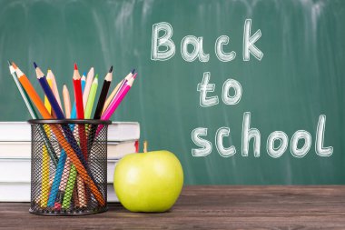 Okul konseptine geri dönelim. Yeşil karatahta kopyalama alanı üzerinde izole edilmiş renkli boyanmış yeşil elma ders kitaplarının yakın plan fotoğrafı