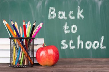 Okul konseptine geri dönelim. Yeşil karatahtaya izole edilmiş renkli kırmızı elmaların ve ders kitaplarının yakın plan fotoğrafı.