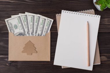 Üstünde dolar dolu el işi bir zarf dolusu dolar ve noel ağacı şekilli kağıt süsleme vardı. Kalem ve dolgun bir kalemi, tahta arka planda, kopyalanmış bir şekilde duruyordu.