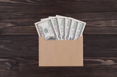 Tepedeki düz manzarada, telif uzayı olan ahşap arka planda izole edilmiş dolarlarla dolu el sanatları zarfının fotoğrafı bulunuyor.